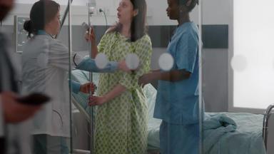 医疗团队帮助生病的女人站床上持有静脉注射流体滴袋